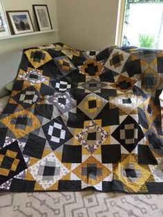 a large black and yellow quilt on a couch in front of a window with pictures