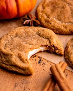 two cookies and an apple on a wooden cutting board with cinnamon sticks next to them