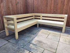 a wooden bench sitting on top of a stone floor next to a fence and wall