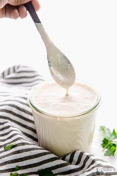 a hand holding a spoon over a jar filled with white liquid and garnished with cilantro