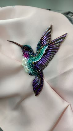 a purple and green bird brooch sitting on top of a white cloth covered pillow