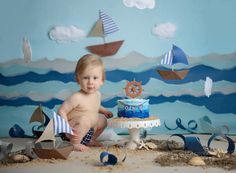 a baby sitting on the floor next to a cake with sailboats in the background