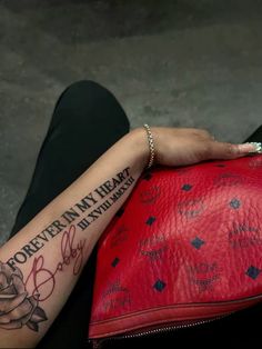 a woman's arm with writing on it and a red purse in front of her