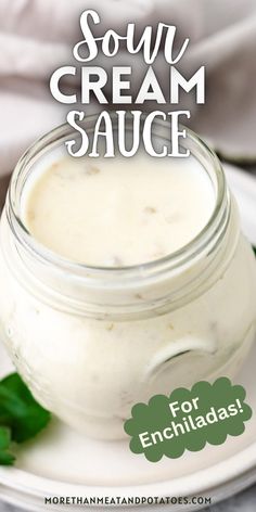 a jar of sour cream sauce sitting on top of a white plate with green leaves