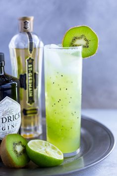 a green drink with kiwi slices on the side and a bottle of gin next to it