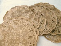 several lace doily are laying on a white tablecloth, one is brown and the other is beige