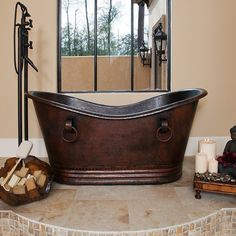 a bath tub sitting on top of a stone floor next to a mirror and candles