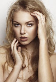 a woman with long blonde hair posing for the camera and holding her hand on her head