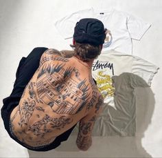 a man with tattoos on his back sitting in front of two t - shirt designs