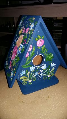 a blue birdhouse with flowers painted on it's side sitting on a table