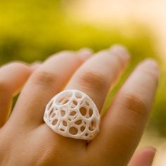 a woman's hand holding a white ring with holes in it and trees in the background