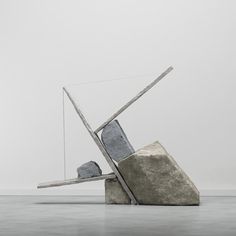 an artistic sculpture made out of rocks and wire on the floor with a white wall in the background