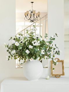 a vase filled with white flowers sitting on top of a table next to a mirror