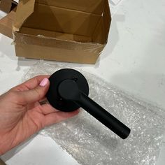 a hand is holding a black object in front of a cardboard box on the table