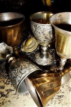 three silver cups sitting on top of a table next to other metal cups and spoons