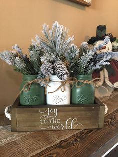 two mason jars with pine cones are sitting on top of a wooden box that says joy to the world