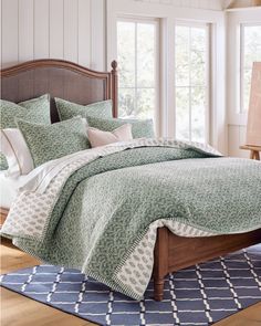 a bed with green and white bedspread in a bedroom next to windows on a rug