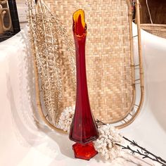 a red vase sitting on top of a white table next to a wicker chair