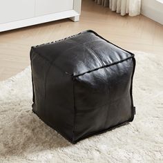 a black leather square ottoman sitting on top of a white rug in a living room