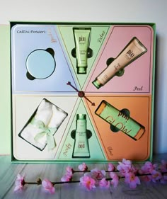 an assortment of beauty products displayed in a box on top of a wooden table next to pink flowers