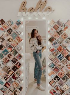 a woman standing in front of a mirror with many pictures on the wall behind her