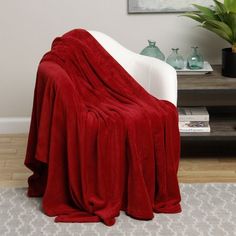 a red blanket sitting on top of a white chair next to a potted plant