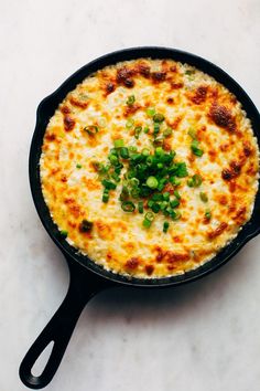 a skillet filled with cheese and green onions on top of a white countertop