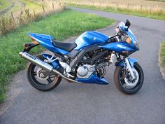 a blue motorcycle parked on the side of a road next to a lush green field