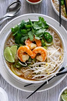 a bowl of shrimp noodle soup with cilantro and limes on the side