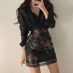 a woman taking a selfie while wearing a dress with flowers on the skirt and black shirt