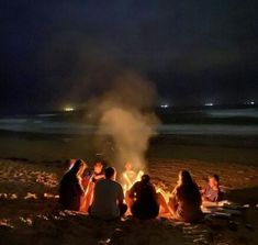 people sitting around a campfire on the beach at night with their backs turned to the camera