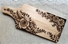 a wooden cutting board decorated with flowers and leaves on a lace tableclothed surface