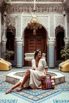 a woman sitting on the ground in front of a building holding a purse and smiling