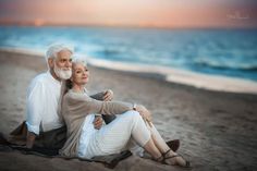 an older couple sitting on the beach at sunset