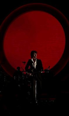 a man sitting in front of a red circle with drums on the ground behind him