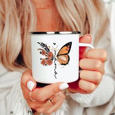 a woman holding a coffee mug with a butterfly on it's side and flowers painted on the inside