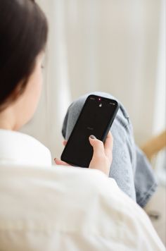 a woman laying in bed while looking at her cell phone with the back turned to the camera