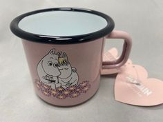 a pink coffee mug with a cartoon character on it and a heart shaped mirror next to it