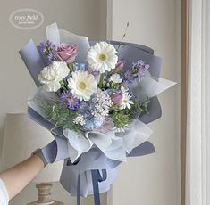 a bouquet of flowers is being held by a woman's hand near a vase