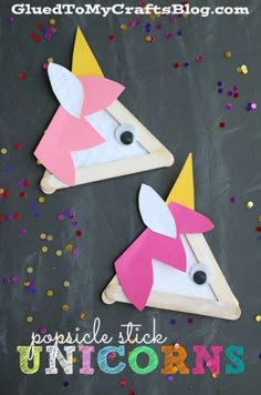 two unicorns made out of popsicle sticks on top of a blackboard with confetti