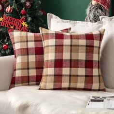 two plaid pillows on a white couch in front of a christmas tree with red and gold decorations