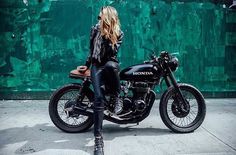 a woman sitting on top of a motorcycle in front of a wall with graffiti written on it