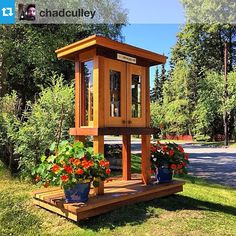 a wooden clock tower sitting on top of a lush green field next to flowers and trees