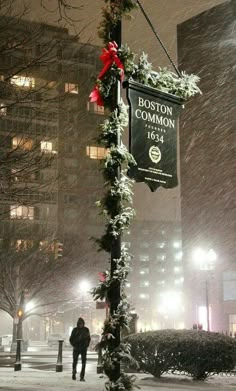 a street sign covered in snow next to a tall building with lights on it's sides