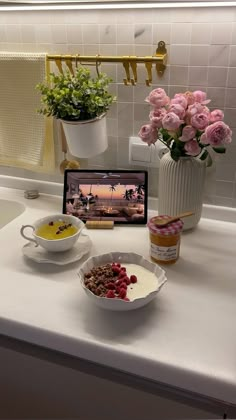 a white counter topped with bowls filled with food next to a laptop computer and flowers