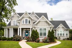 a house with white trim and blue door surrounded by green grass, shrubs and trees