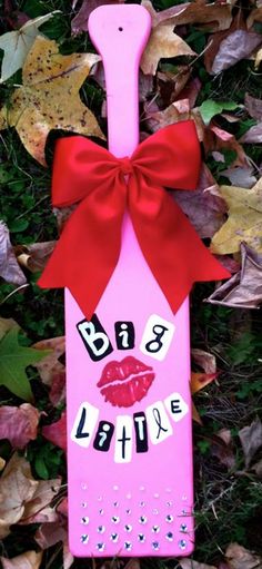 a pink bottle with a red bow on it sitting in the grass next to leaves