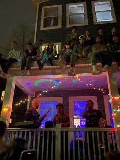 a group of people sitting on the roof of a house with christmas lights all around them