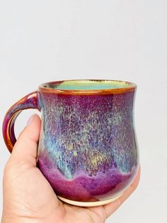 a hand holding a purple and blue coffee cup