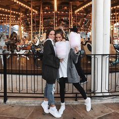 two young women standing in front of a carousel at a park with pink cotton candy